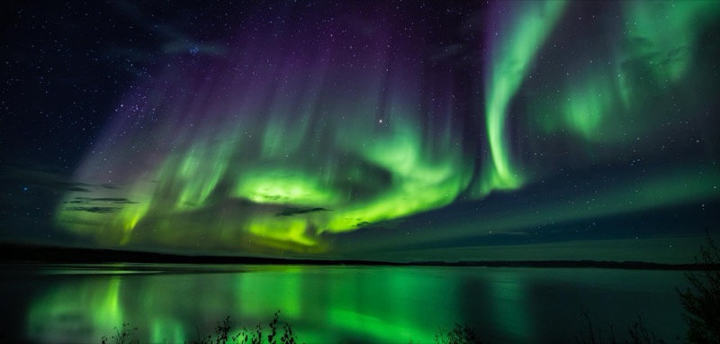 Aurora boreal verde reflejada en un lago helado cerca de Yellowknife