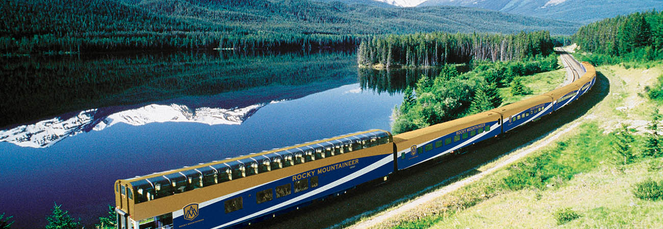 Tren Rocky Mountaineer con vagones panorámicos junto a un lago espejo en las Rocosas